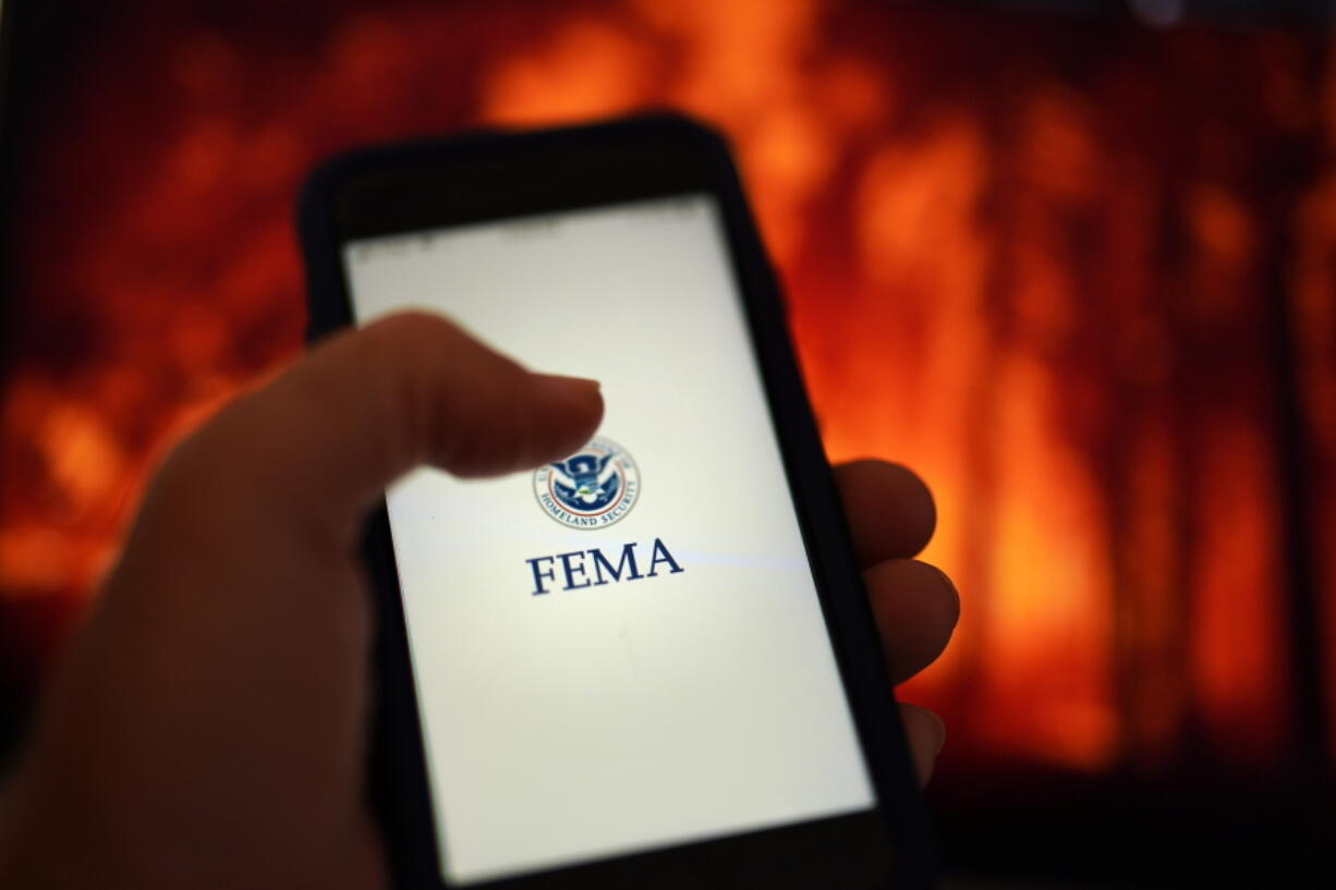 A phone loads the Federal Emergency Management Agency application with the background of an image of a fire on Wednesday, June 29, 2022, in San Diego. FEMA is releasing the largest update to its mobile application in a decade, at the beginning of a hurricane season that experts predict will be above average and a wildfire season that's on par with recent years' big burns.