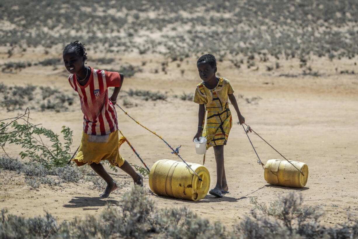 FILE - Young girls pull containers of water during a drought as they return to their huts from a well in the village of Lomoputh in northern Kenya on, May 12, 2022. Better climate-related research and early weather warning systems are needed as extreme weather -- from cyclones to drought -- continues to inflict the African continent, said the Sudanese billionaire and philanthropist Mo Ibrahim, who heads up his own foundation.