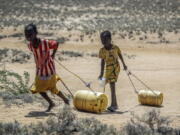 FILE - Young girls pull containers of water during a drought as they return to their huts from a well in the village of Lomoputh in northern Kenya on, May 12, 2022. Better climate-related research and early weather warning systems are needed as extreme weather -- from cyclones to drought -- continues to inflict the African continent, said the Sudanese billionaire and philanthropist Mo Ibrahim, who heads up his own foundation.