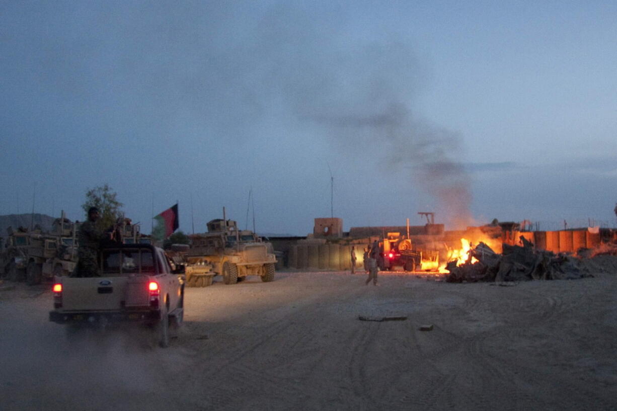 FILE - An Afghan National Army pickup truck passes parked U.S. armored military vehicles, as smoke rises from a fire in a trash burn pit at Forward Operating Base Caferetta Nawzad, Helmand province south of Kabul, Afghanistan, April 28, 2011. The Senate is expected to approve on Thursday a large expansion of health care and disability benefits for veterans of Iraq and Afghanistan in response to concerns about their exposure to toxic burn pits.