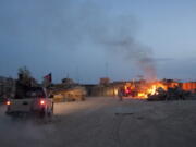 FILE - An Afghan National Army pickup truck passes parked U.S. armored military vehicles, as smoke rises from a fire in a trash burn pit at Forward Operating Base Caferetta Nawzad, Helmand province south of Kabul, Afghanistan, April 28, 2011. The Senate is expected to approve on Thursday a large expansion of health care and disability benefits for veterans of Iraq and Afghanistan in response to concerns about their exposure to toxic burn pits.