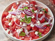 This image shows a recipe for watermelon feta salad topped with thinly sliced red onion and mint leaves.