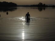 FILE - A man walks in the water as the sun rises above the Miribel lake, outside Lyon, central France, Saturday, June 18, 2022. A heat wave that's already lasted more than a week keeps on baking the US, Asia, Europe and even the Arctic.