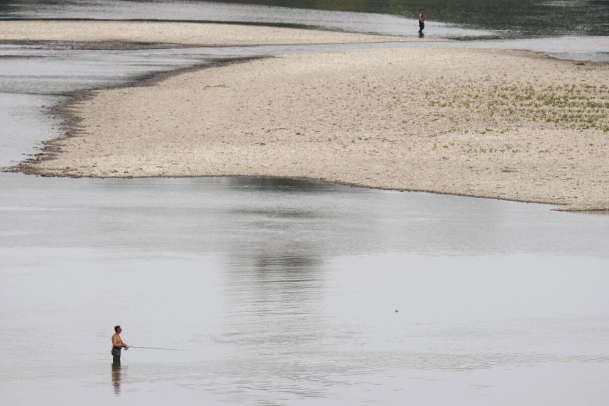 FILE - People fish near a hydroelectric power plant at Isola Serafini, on the Po river in San Nazzaro, Italy, Wednesday, June 15, 2022. The drying up of the river is jeopardizing drinking water in Italy's densely populated and highly industrialized districts and threatening irrigation in the most intensively farmed part of the country. The mayor of Milan signed an ordinance Saturday, June 25, 2022, turning off public decorative fountains and limiting water sprinklers in Italy's business capital as northern Italy endures one of the worst droughts in decades.