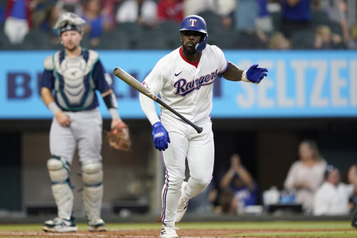 Texas Rangers' Adolis Garcia, right, tosses his bat in front of Seattle Mariners catcher Cal Raleigh, left, after hitting a three-run home run during the fourth inning of a baseball game in Arlington, Texas, Saturday, June 4, 2022. Rangers' Marcus Semien and Mitch Garver also scored on the play.