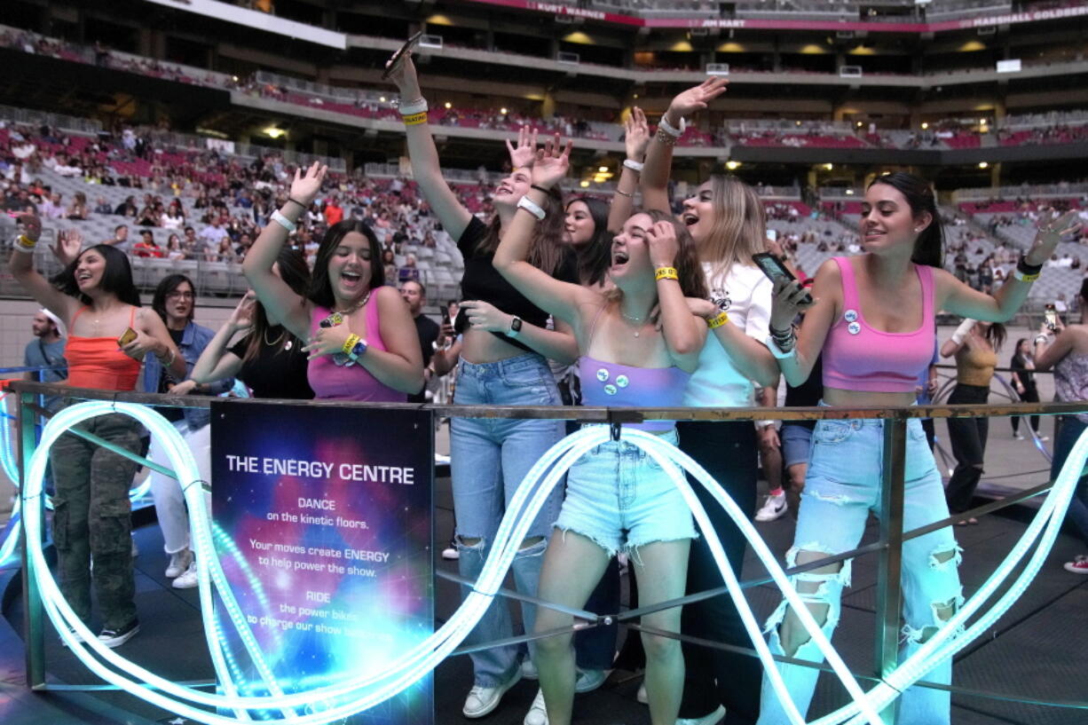 Concertgoers dance during Coldplay's Music of the Spheres world tour on Thursday, May 12, 2022, at State Farm Stadium in Glendale, Ariz. The band has included energy-storing stationary bikes to their latest world tour, encouraging fans to help power the show as part of a push to make the tour more environmentally friendly.