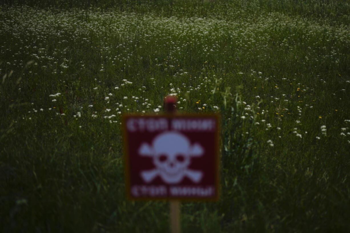 Flowers in a field near a poster warning about mines in Lypivka, on the outskirts of Kyiv, Ukraine, Tuesday, June 14, 2022. Russia's invasion of Ukraine is spreading a deadly litter of mines, bombs and other explosive devices that will endanger civilian lives and limbs long after the fighting stops.