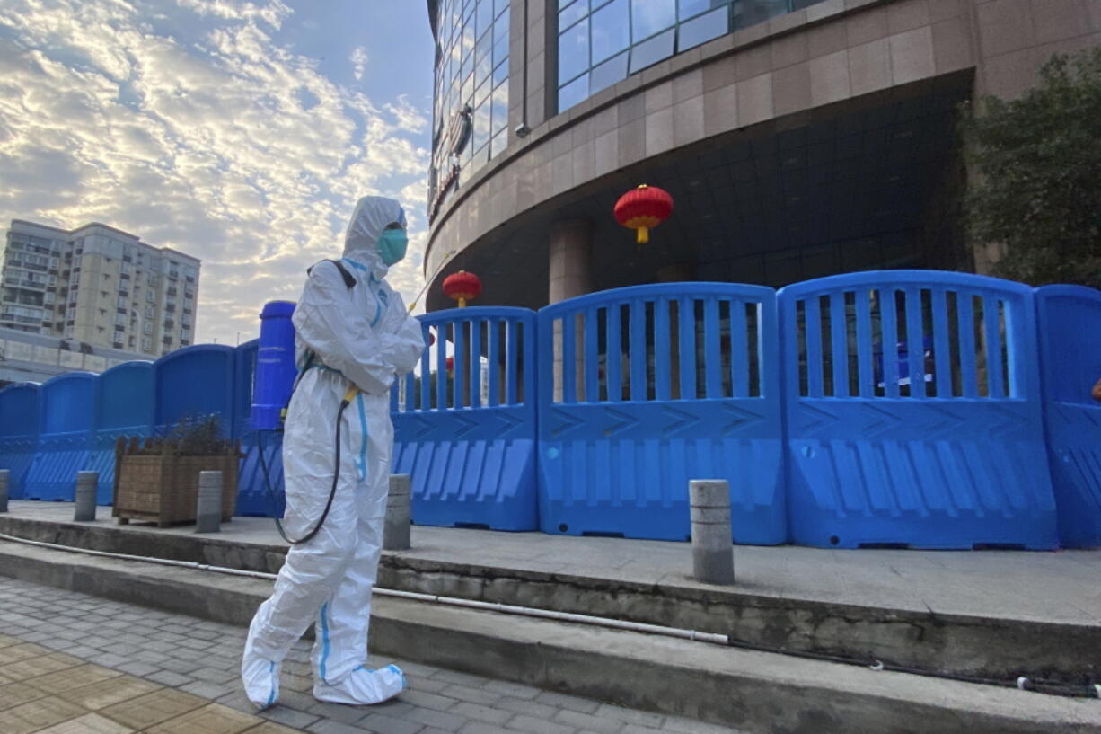 FILE - A worker in protectively overalls and carrying disinfecting equipment walks outside the Wuhan Central Hospital, China on  Feb. 6, 2021.