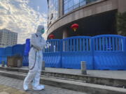 FILE - A worker in protectively overalls and carrying disinfecting equipment walks outside the Wuhan Central Hospital, China on  Feb. 6, 2021.