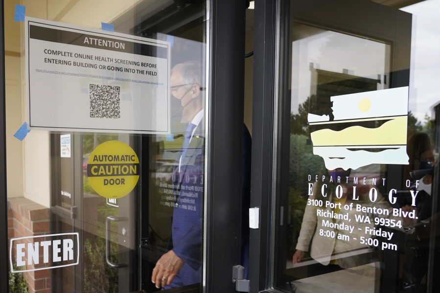 Washington Gov. Jay Inslee walks past a sign asking visitors to complete a health screening as he steps outside to talk to reporters, Thursday, June 2, 2022, at a Dept. of Ecology office in Richland, Wash. On May 25, 2022, Inslee's office said the Governor had tested positive for COVID-19. Inslee, who has recently criticized the slow pace of cleaning up the Hanford Nuclear Reservation in Washington state, was speaking ahead of a scheduled tour of the nuclear weapons production site and repeated his message that more federal money is needed to finish the job. (AP Photo/Ted S.