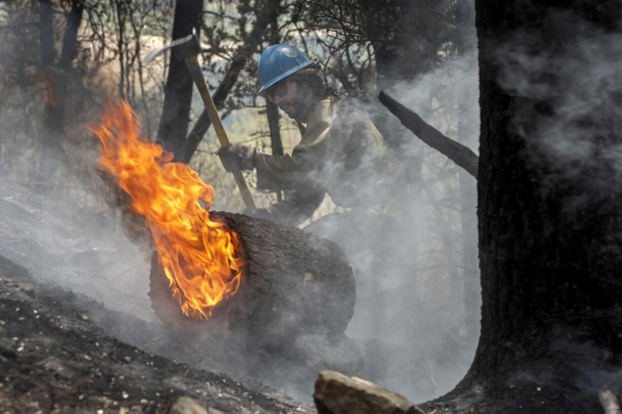 FILE - Carson Hot Shots Tyler Freeman works to keep a burning log from rolling down a slope, May 23, 2022, as he and his co-workers work on hot spots from the Calf Canyon/Hermits Peak Fire in the Carson National Forest west of Chacon, N.M. The U.S. Forest Service is acknowledging multiple miscalculations, inaccurate models and a lack of understanding of just how dry things are in the Southwest in a review of a planned burn that turned into the largest blaze in New Mexico's recorded history. The agency on Tuesday, June 21, 2022, released the findings after investigating the decisions that led up to igniting a prescribed fire that was meant to remove vegetation in an effort to reduce the wildfire threat in the Sangre de Cristo mountain range in northern New Mexico.