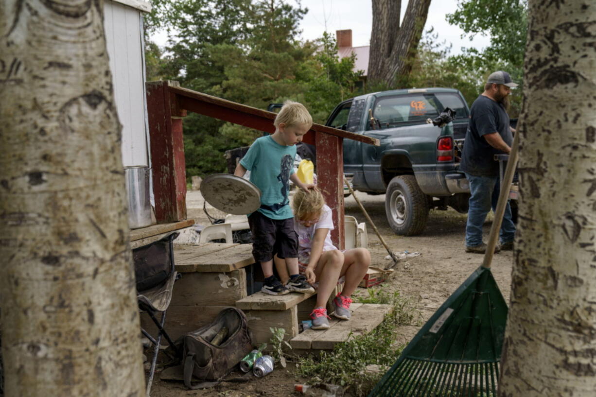 CORRECTS SPELLING OF FIRST NAME TO HARLEE INSTEAD OF HARLEY - Harlee Holmes, 8, right, helps her brother Creek, 3, put his shoes on as the family packs up to leave their home that was damaged by severe flooding in Fromberg, Mont., Friday, June 17, 2022.