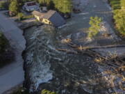 FILE - A house sits in Rock Creek after floodwaters washed away a road and a bridge in Red Lodge, Mont., on June 15, 2022. Yellowstone National Park is reopening its flood-damaged north loop at noon on Saturday, July 2, 2022, in time for the Fourth of July holiday weekend. Park officials say the roads from Norris Junction to Mammoth Hot Springs, to Tower-Roosevelt, to Canyon Junction and back to Norris Junction will be open. The loop is reopening nearly three weeks after massive flooding forced thousands to flee the park as water, rocks and mud washed out bridges and roads.