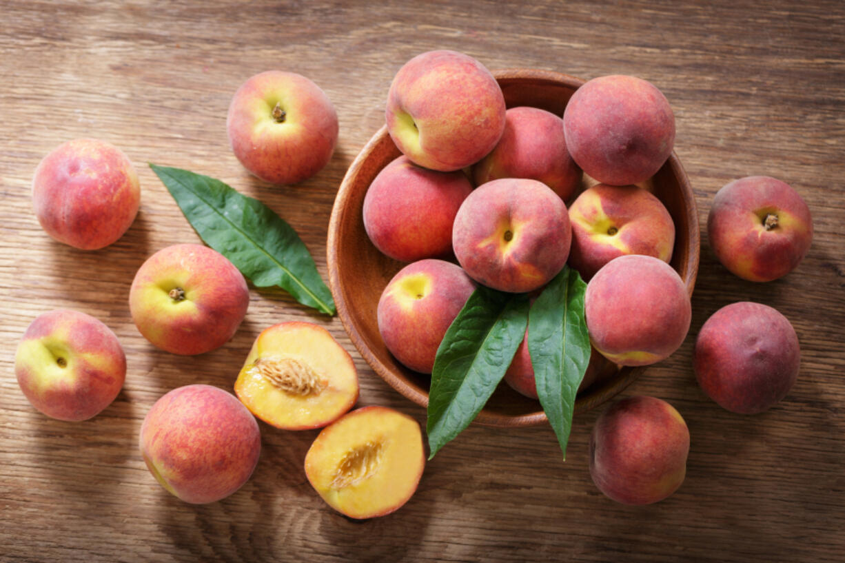 Fresh ripe peaches in a bowl on a wooden table, top view (iStock.com)