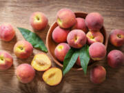 Fresh ripe peaches in a bowl on a wooden table, top view (iStock.com)