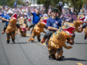 People in inflatable dinosaur costumes march down Pioneer Street on Monday, July 4, 2022, during a Fourth of July parade in downtown Ridgefield.