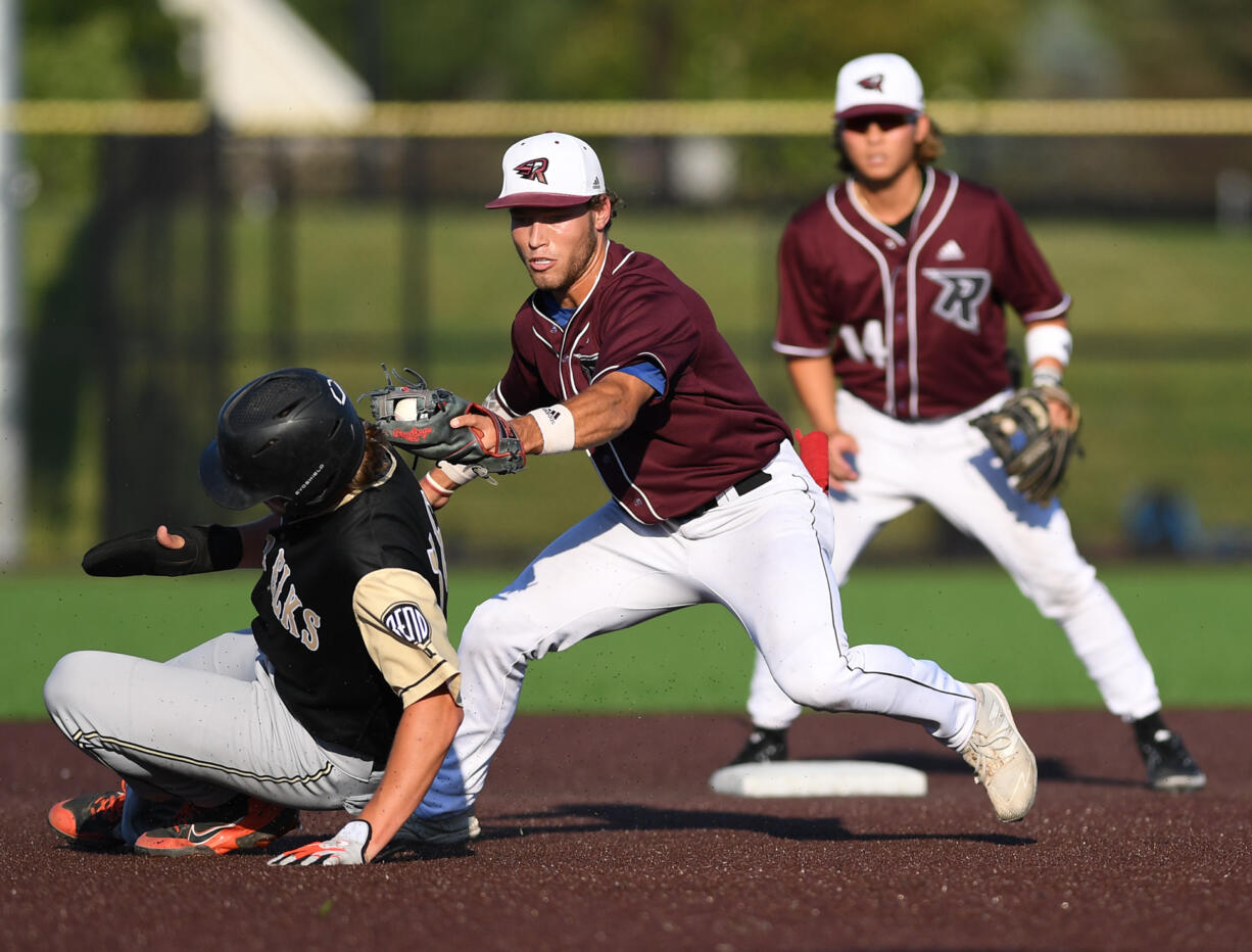 Raptors shortstop Travis Welker, center, tags out Elks outfielder Brady Kasper, left, as Raptors second baseman Jake Tsukada, right, looks on Tuesday, July 26, 2022, during a game between Ridgefield and the Bend Elks at the Ridgefield Outdoor Recreation Complex.