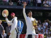 Serbia's Novak Djokovic, right, holds the winners trophy as he celebrates after beating Australia's Nick Kyrgios, left, to win the final of the men's singles on day fourteen of the Wimbledon tennis championships in London, Sunday, July 10, 2022.