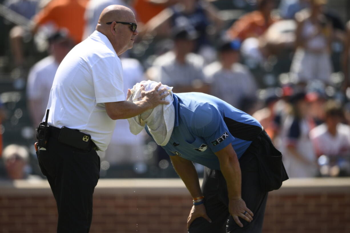 Baltimore Orioles head trainer Brian Ebel, left, helps home plate umpire Scott Barry get relief with a wet towel around his head after the sixth inning of a baseball game between the Orioles and the New York Yankees, Sunday, July 24, 2022, in Baltimore. The Yankees won 5-0.