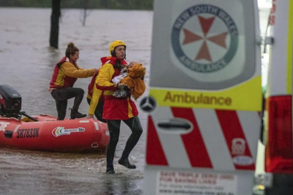 In this photo provided by the State Emergency Service, surf lifesaver Lee Archer carries a baby as the child and the mother are rescued from flood waters in Bulga, Australia, Wednesday, July, 6, 2022. Floodwaters were receding in Sydney and its surrounds on Thursday, July 7, 2022, as heavy rain continued to threaten to inundate towns north of Australia's largest city.