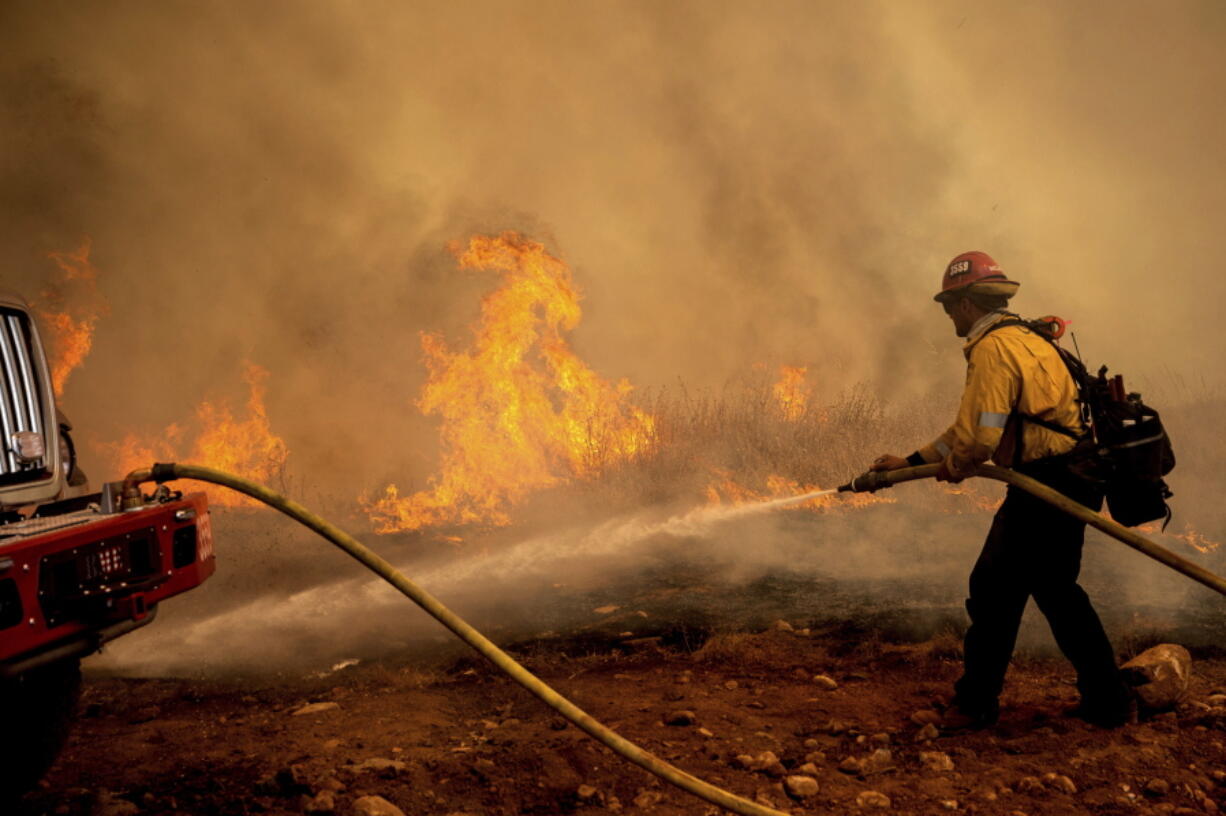 A firefighter sprays water while trying to keep the Electra Fire from spreading in the Pine Acres community of Amador County, Calif., on Tuesday, July 5, 2022.