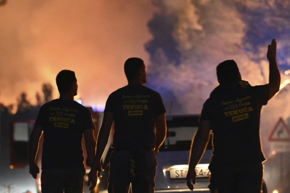 Firefighters watch a wildfire burning near Zaton, Croatia, Wednesday, July 13, 2022. Fueled by strong winds, fires raged at Croatia's Adriatic Sea, with the most dramatic situation reported near the town of Sibenik, where water-dropping planes and dozens of firefighters struggled to contain the flames that briefly engulfed some cars and the church tower in the Zaton area on the outskirts of the town before firefighters managed to put it out.