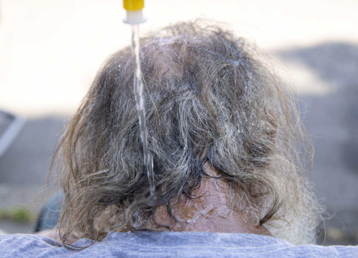 Maggy Johnston, ARCHES outreach coordinator, squeezes water on a man's head during a heat wave with temperatures reaching 100 degrees in Salem, Ore., Tuesday, July 26, 2022.