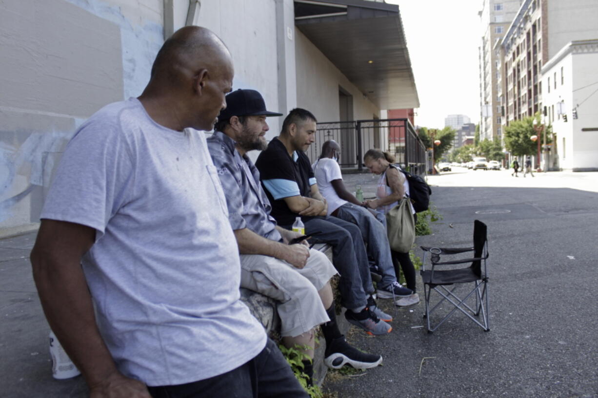 William Nonluecha, foreground, and his friends sit in the shade, Wednesday, July 27, 2022, in Portland, Ore., as a heat wave envelopes the Pacific Northwest. Nonluecha, who lives in a tent, says the heat becomes unbearable inside it when temperatures rise and he stays cool by going to public libraries and riding public transit. "I got a flier yesterday ... about the cooling shelter but it was too late," Nonluecha says.