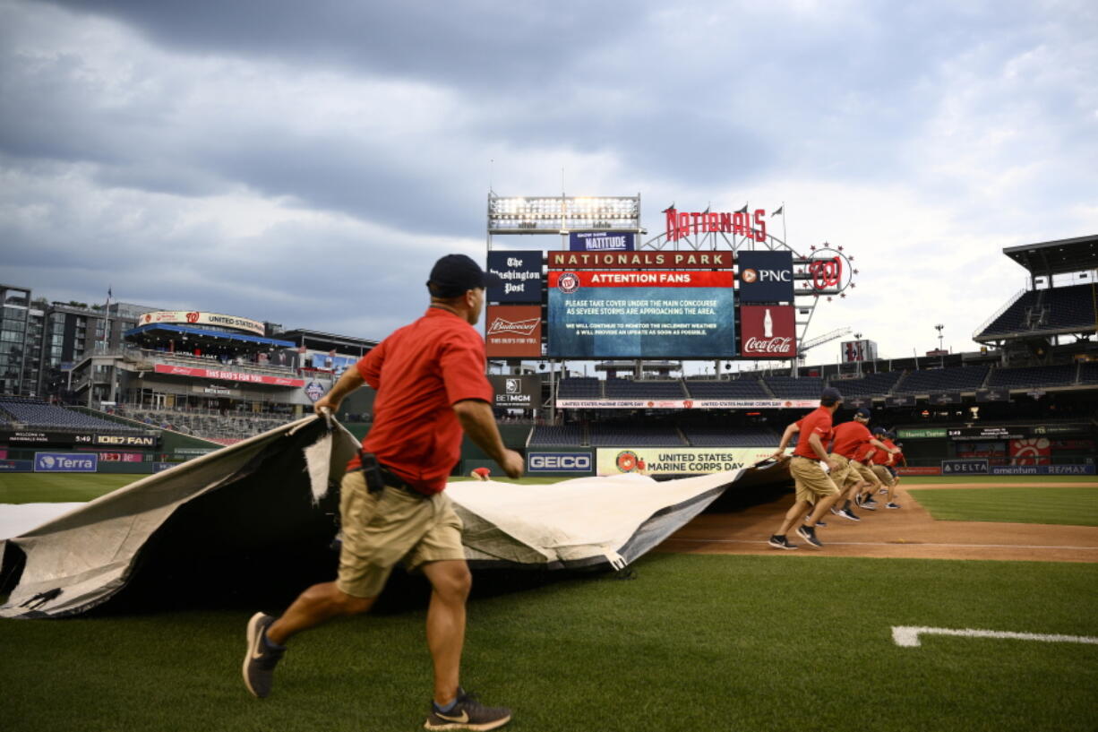 The scoreboard warns of inclement weather in the area as the Washington Nationals grounds crew rolls out the tarp on the field before a baseball game between the Nationals and the Seattle Mariners, Tuesday, July 12, 2022, in Washington.