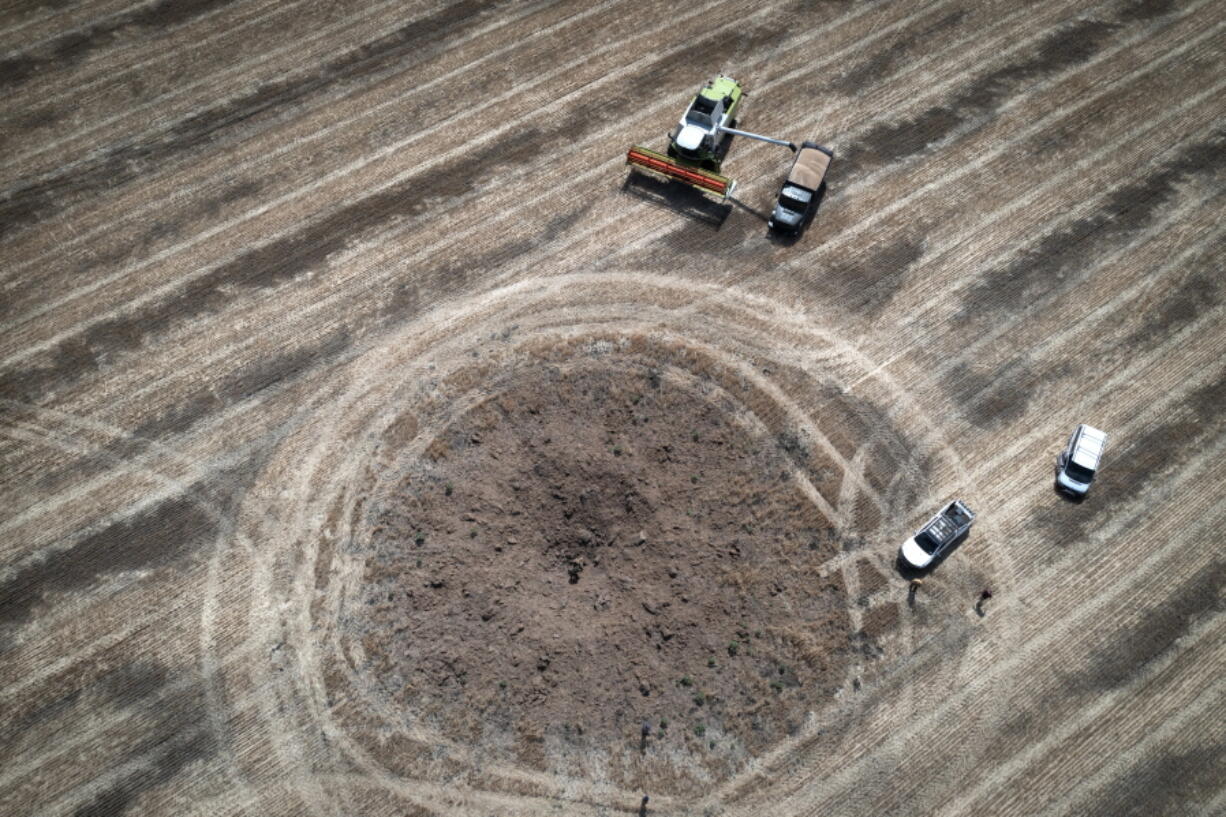 A farmer collects harvest on a field ten kilometres from the front line where fierce battle is going, a crater left by the Russian rocket in the foreground, in the Dnipropetrovsk region, Ukraine, Monday, July 4, 2022. An estimated 22 million tons of grain are blocked in Ukraine, and pressure is growing as the new harvest begins. The country usually delivers about 30% of its grain to Europe, 30% to North Africa and 40% to Asia. But with the ongoing Russian naval blockade of Ukrainian Black Sea ports, millions of tons of last year's harvest still can't reach their destinations.