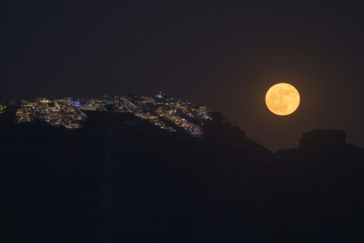 FILE - The strawberry supermoon rises behind the village of Imerovigli on Sandorini's caldera, in Greece's Cyclades islands, on June 14, 2022. If you missed last month's supermoon, you have another chance. This month's full moon is Wednesday, July 13, 2022. At the same time, the moon's orbit will bring it closer to Earth than usual. This cosmic combo is called a supermoon.