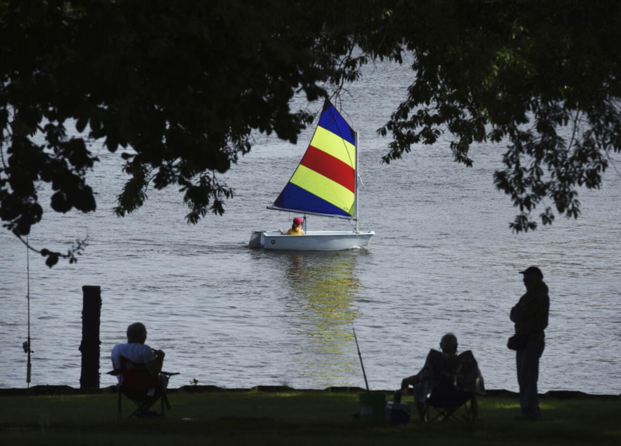 FILE - A sailor with the St. Joseph Junior Foundation Summer Sailling School cruises past fishermen along the St. Joseph River in St. Joseph, Mich., Wednesday, June 15, 2022.  The fast-changing coronavirus has kicked off summer in the U.S. with lots of infections but relatively few deaths compared to its prior incarnations. COVID-19 is still killing hundreds of Americans each day, but for many people the virus is not nearly as dangerous as it was.