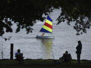 FILE - A sailor with the St. Joseph Junior Foundation Summer Sailling School cruises past fishermen along the St. Joseph River in St. Joseph, Mich., Wednesday, June 15, 2022.  The fast-changing coronavirus has kicked off summer in the U.S. with lots of infections but relatively few deaths compared to its prior incarnations. COVID-19 is still killing hundreds of Americans each day, but for many people the virus is not nearly as dangerous as it was.