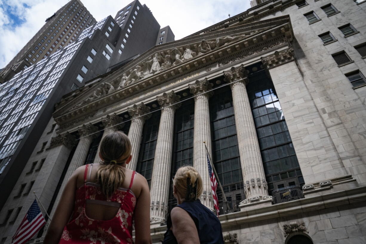 FILE - Pedestrians pass the New York Stock Exchange on July 14, 2022, in New York. The U.S. economy is caught in an awkward, painful place. A confusing one, too. Growth appears to be sputtering, home sales are tumbling and economists warn of a potential recession ahead. But consumers keep spending, businesses keep posting profits and the economy keeps adding hundreds of thousands of jobs a month.