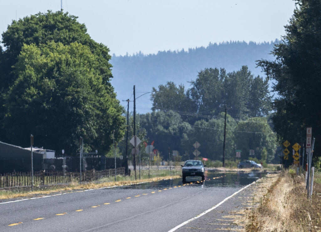 A car drives along Washington State Route 501 as a mirage makes the road appear covered in water on Tuesday, Aug. 30, 2022. Temperatures soared into the upper 90s on Tuesday after a cool weekend and are expected to remain high throughout the week.