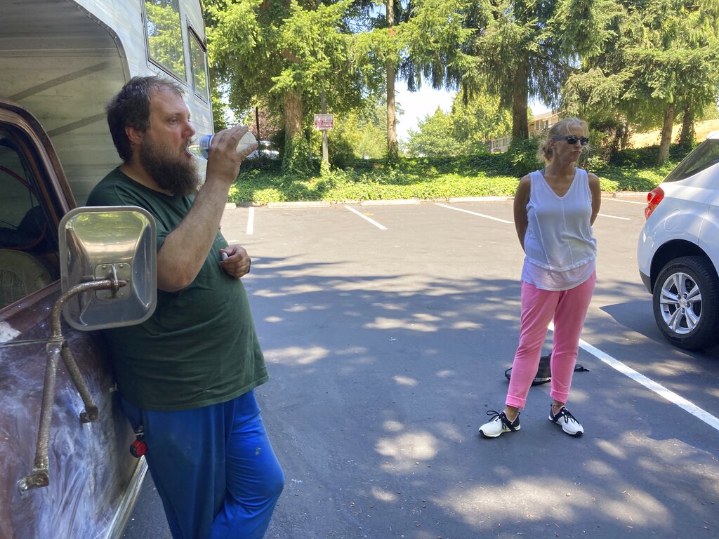 Orson Lee, who's been homeless for six years, drinks water from a water bottle while outreach worker Mary Guiberson looks on at a park in Burien, Wash. The National Weather Service extended its heat advisory by one more day in the Seattle area. Outreach teams have fanned out to provide water and other aid to the homeless.