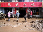 In this photo released by Xinhua News Agency, residents clear sludge from their property in the aftermath of floods in Qingshan Township of Datong Hui and Tu Autonomous County in northwest China's Qinghai Province on Thursday, Aug. 18, 2022. A sudden rainstorm in western China triggered a landslide that diverted a river and caused flash flooding in populated areas, killing some and leaving others missing, Chinese state media said Thursday.