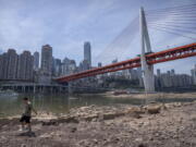 A man walks along the lower than normal bank of the Jialing River in southwestern China's Chongqing Municipality, Friday, Aug. 19, 2022. Ships crept down the middle of the Yangtze on Friday after the driest summer in six decades left one of the mightiest rivers shrunk to barely half its normal width and set off a scramble to contain damage to a weak economy in a politically sensitive year.