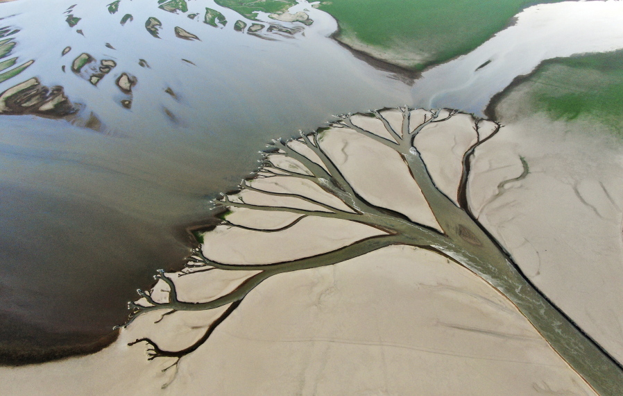 In this aerial photo released by China's Xinhua News Agency, water flows through chanels in the lake bed of Poyang Lake, China's largest freshwater lake, in eastern China's Jiangxi Province, Monday, Aug. 22, 2022. With China's biggest freshwater lake reduced to just 25% of its usual size by drought, work crews are digging trenches to keep water flowing to irrigate crops.