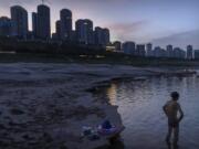 A man stands in shallow water near the dry riverbed of the Yangtze River in southwestern China's Chongqing Municipality, Friday, Aug. 19, 2022. Ships crept down the middle of the Yangtze on Friday after the driest summer in six decades left one of the mightiest rivers shrunk to barely half its normal width and set off a scramble to contain damage to a weak economy in a politically sensitive year.