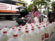 Vanessa Correa, left, and Gigi Fiske, right, pass out gallons of milk at a food distribution held by the Farm Share food bank, Wednesday, July 20, 2022, in Miami. Long lines are back at food banks around the U.S. as working Americans overwhelmed by inflation turn to handouts to help feed their families.