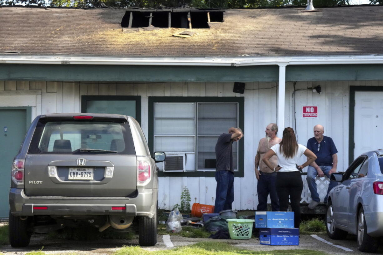 Neighbors stand around a multi-room renting facility in the aftermath of a fatal shooting in Houston on Sunday, Aug. 28, 2022. A longtime tenant started several fires at the site early Sunday and then shot at residents as they fled the blaze, before authorities fatally shot him, police said.