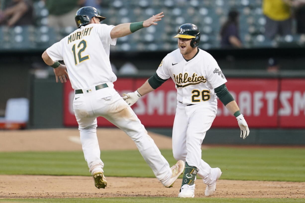 Oakland Athletics' Sheldon Neuse (26) is congratulated by Sean Murphy (12) after hitting into a fielder's choice that scored Tony Kemp during the 10th inning of a baseball game against the Seattle Mariners in Oakland, Calif., Saturday, Aug. 20, 2022.