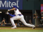 Texas Rangers' Bubba Thompson, left, hits a sacrifice bunt in front of Seattle Mariners catcher Cal Raleigh during the fourth inning of a baseball game in Arlington, Texas, Saturday, Aug. 13, 2022. Rangers' Charlie Culberson scored on the play.