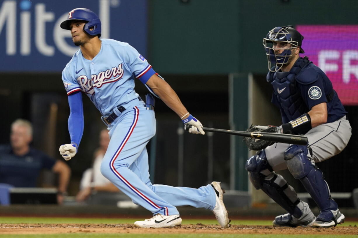 Texas Rangers' Bubba Thompson, left, and Seattle Mariners catcher Curt Casali (5) watch Thompson's single that drove in two runs during the fourth inning of a baseball game in Arlington, Texas, Sunday, Aug. 14, 2022. Rangers' Meibrys Viloria and Nathaniel Lowe (30) scored on the play.