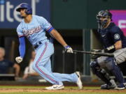 Texas Rangers' Bubba Thompson, left, and Seattle Mariners catcher Curt Casali (5) watch Thompson's single that drove in two runs during the fourth inning of a baseball game in Arlington, Texas, Sunday, Aug. 14, 2022. Rangers' Meibrys Viloria and Nathaniel Lowe (30) scored on the play.