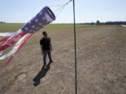 Hay farmer Milan Adams stands in a dry hay field near a wind sock, left, in Exeter, R.I., Tuesday, Aug. 9, 2022. Adams said in prior years it rained in the spring. This year, he said, the dryness started in March, and April was so dry he was nervous about his first cut of hay.