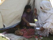 Rubina Bibi, 53, right, sit near to her family after take refuge at a camp after fleeing her flood-hit homes, in Charsadda, Pakistan, Tuesday, Aug. 30, 2022. Disaster officials say nearly a half million people in Pakistan are crowded into camps after losing their homes in widespread flooding caused by unprecedented monsoon rains in recent weeks.