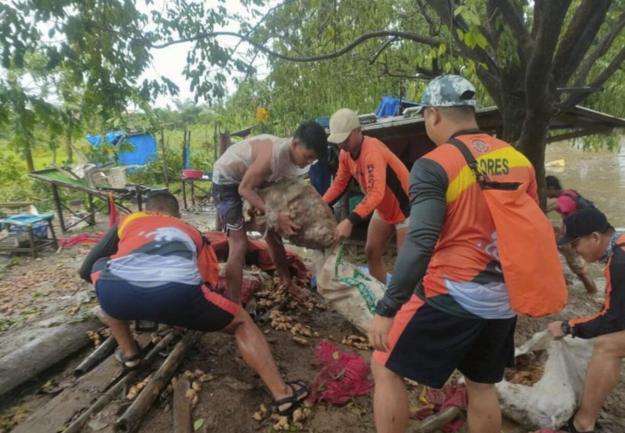 In this photo provided by the Philippine Coast Guard, rescuers carry vegetables as they move them to safer grounds in Tuguegarao, Cagayan province, northern Philippines on Tuesday Aug. 23, 2022. A tropical storm lashed the northern Philippines with strong wind and rain Tuesday, injuring at least two people and prompting the president to close schools and government offices in the capital and outlying provinces.