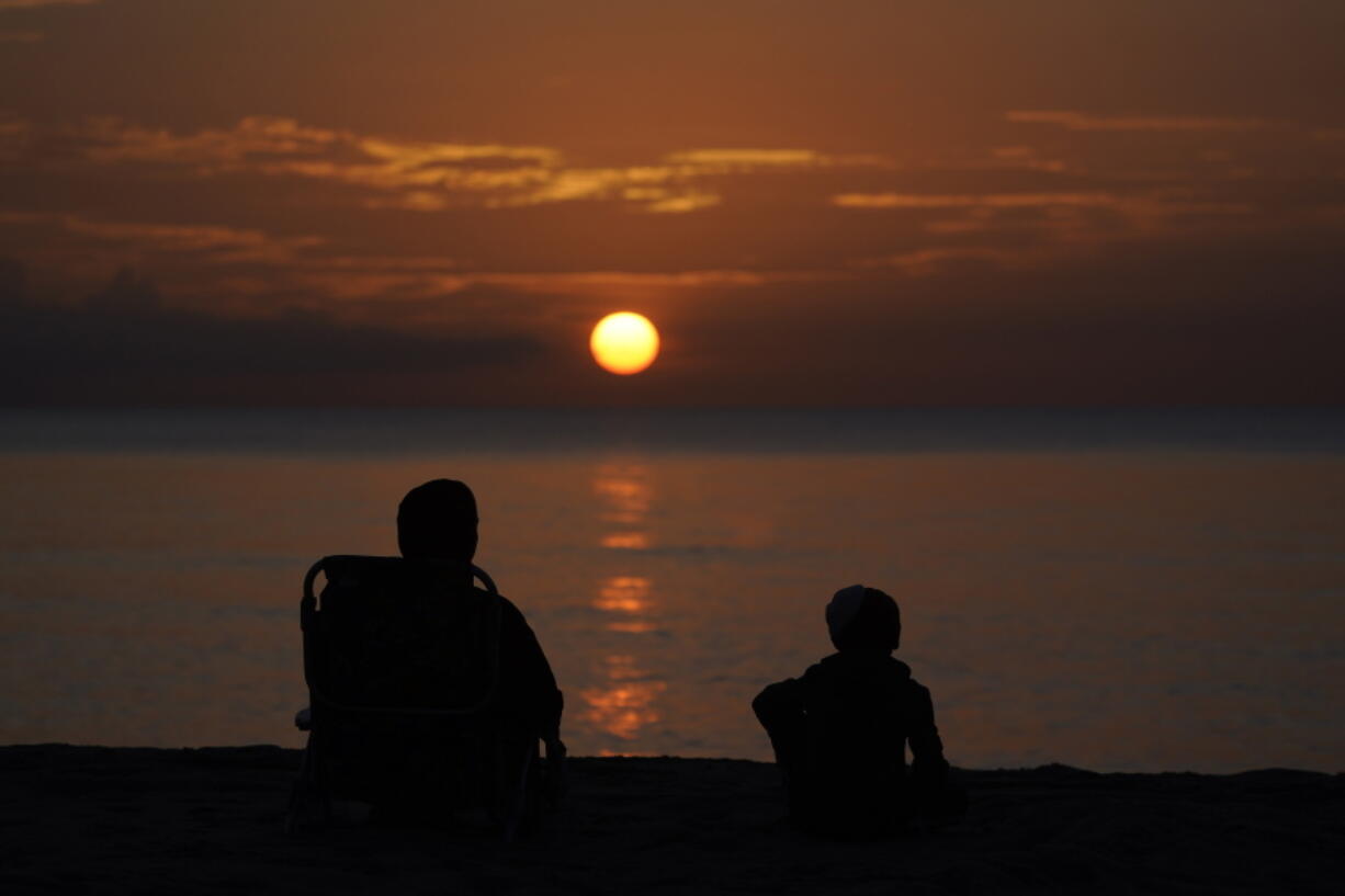 FILE - A pair of beach goers watch the sun rise over the Atlantic Ocean, Friday, June 10, 2022, in Surfside, Fla. All the experts predicted this would be a more active than normal hurricane season, but then nothing happened. Scientists think a persistent patch of dry air is the reason storms aren't forming.